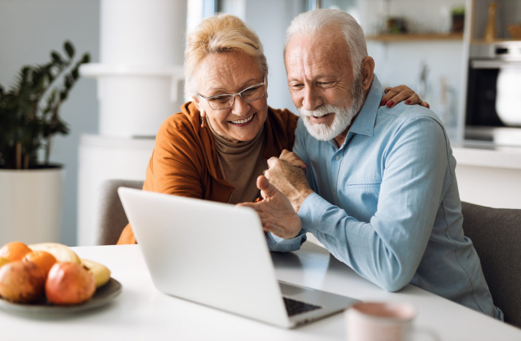 Happy senior couple sitting together at table while using laptop in senior community