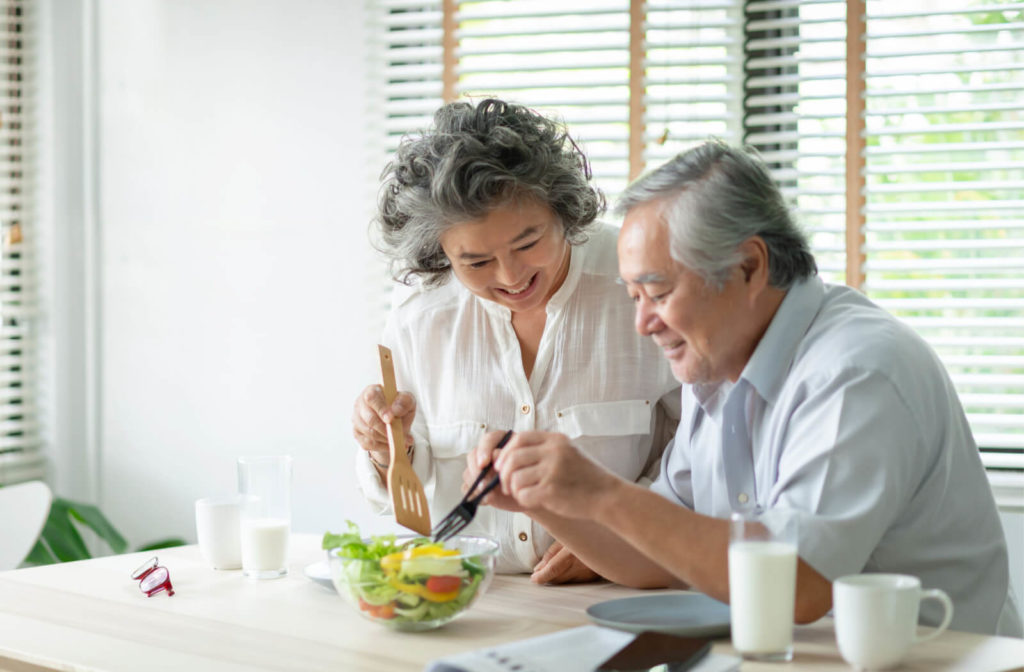 A senior couple preparing and cooking healthy salad at home together. Senior man and woman smiling enjoying a healthy meal.
