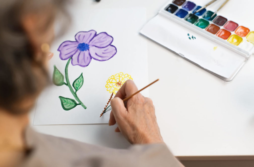 An elderly woman painting flowers with watercolors.