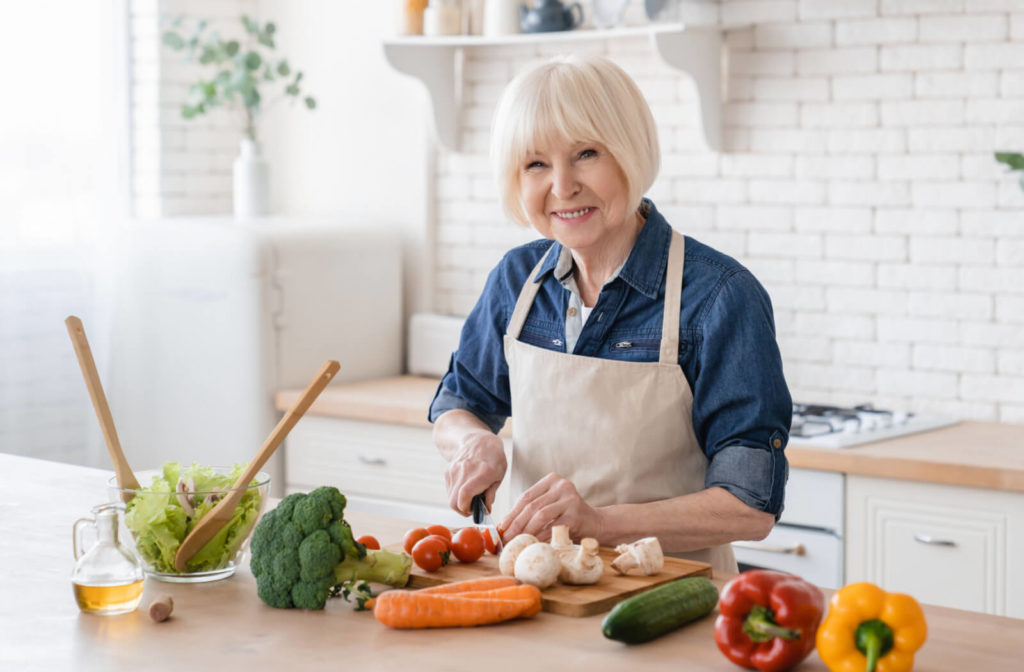 A senior woman with white hair cutting vegetables and preparing a salad.