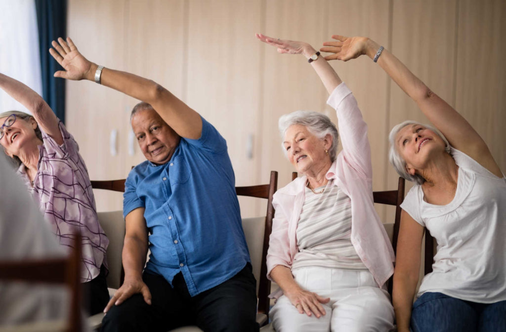 A group of seniors sitting and exercising together in a senior living community.