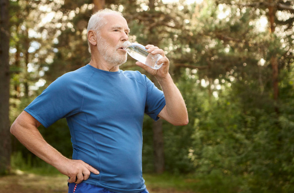 A senior man drinking a bottle of water after doing an exercise in a park.
