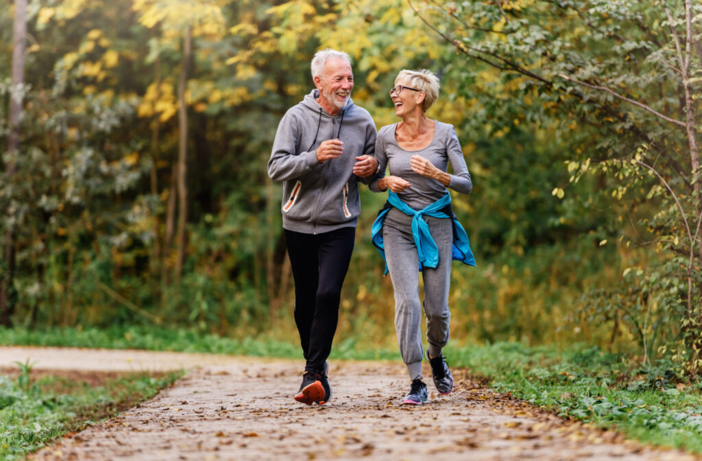 A senior man and a woman smiling while jogging outdoors.