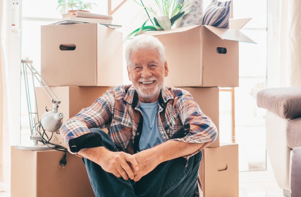 A smiling senior man sitting in front of several boxes as he prepares to move to senior living.