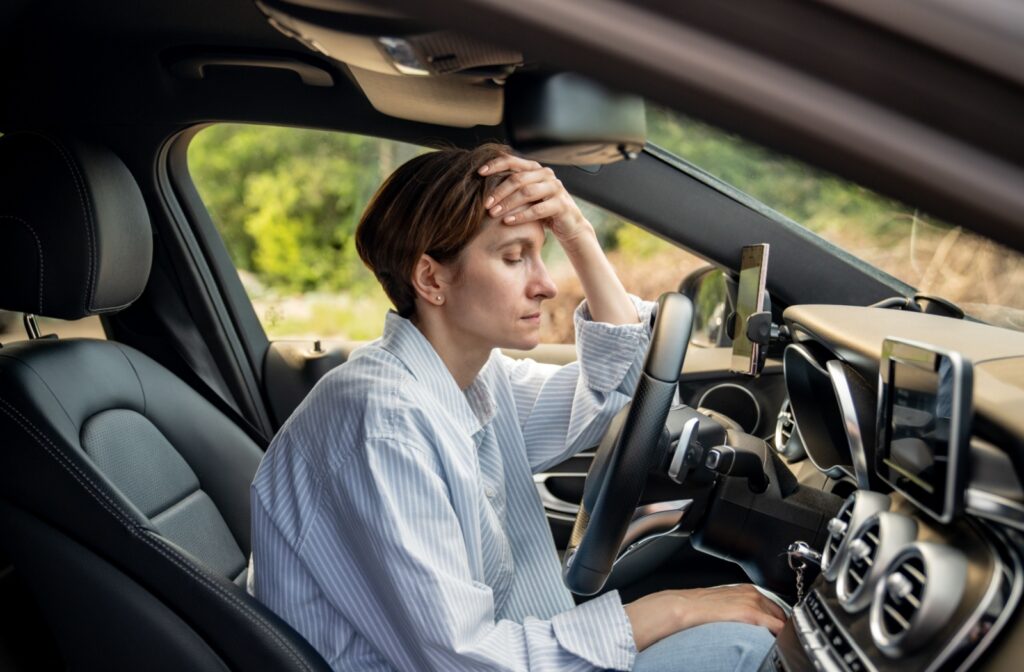 An overwhelming person sitting in their car cradles their head.