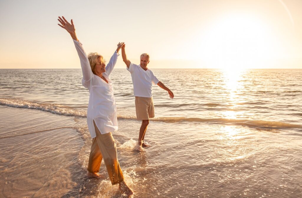 A joyful couple holding hands by the water's edge on the beach, celebrating the beginning of their retirement.