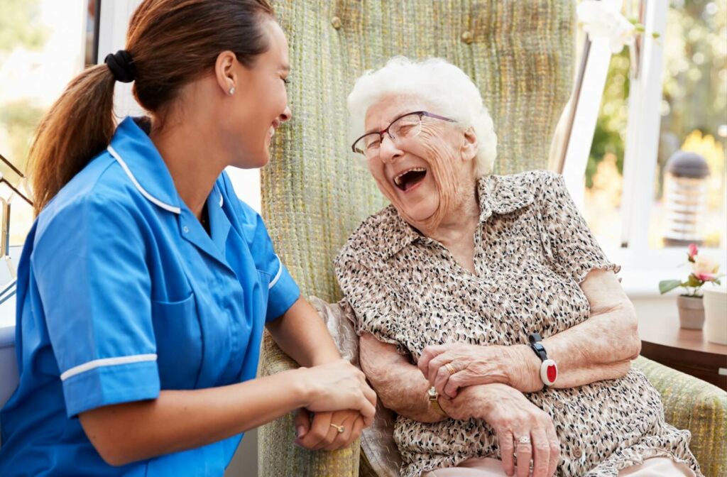 A caregiver in a blue uniform shares a joyful moment with an elderly woman.