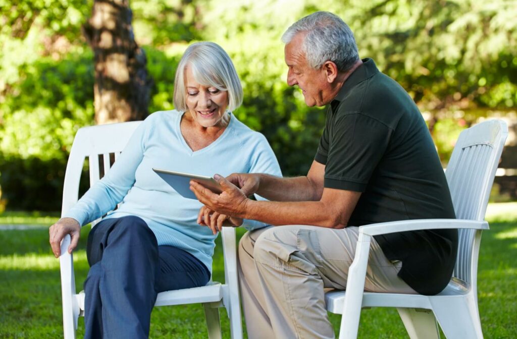 Two seniors in assisted living spend time bonding together outside over pictures on a tablet
