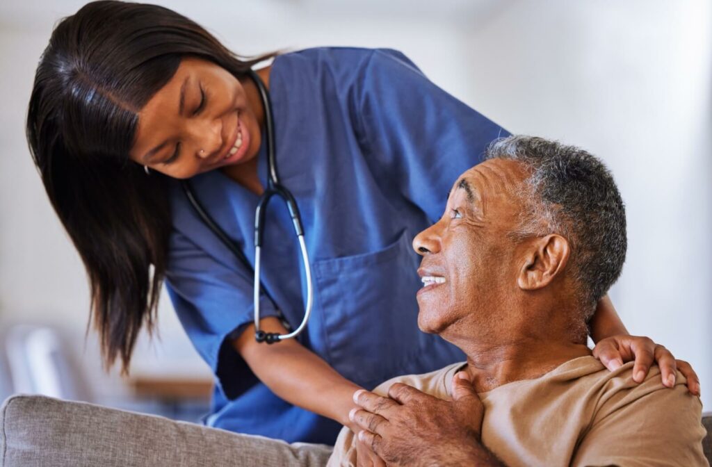 A nurse smiles as they lean over a senior in memory care, using physical touch as an anchor to help check-in with them